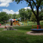Children's park equipment including swings, climbing fort, ladybug ride, carousel and picnic table with bench seating.
