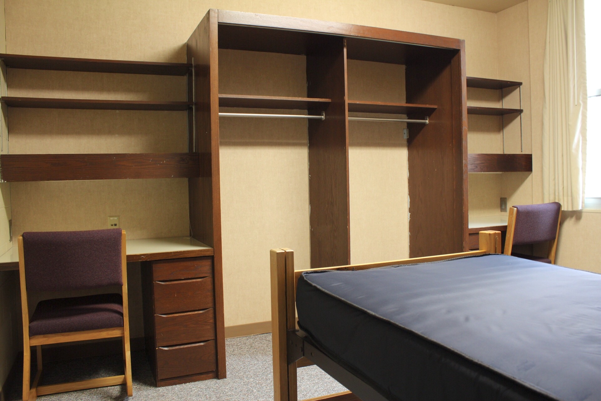 Centennial Complex room with 2 desks, chairs, clothing area and a frame and mattress.