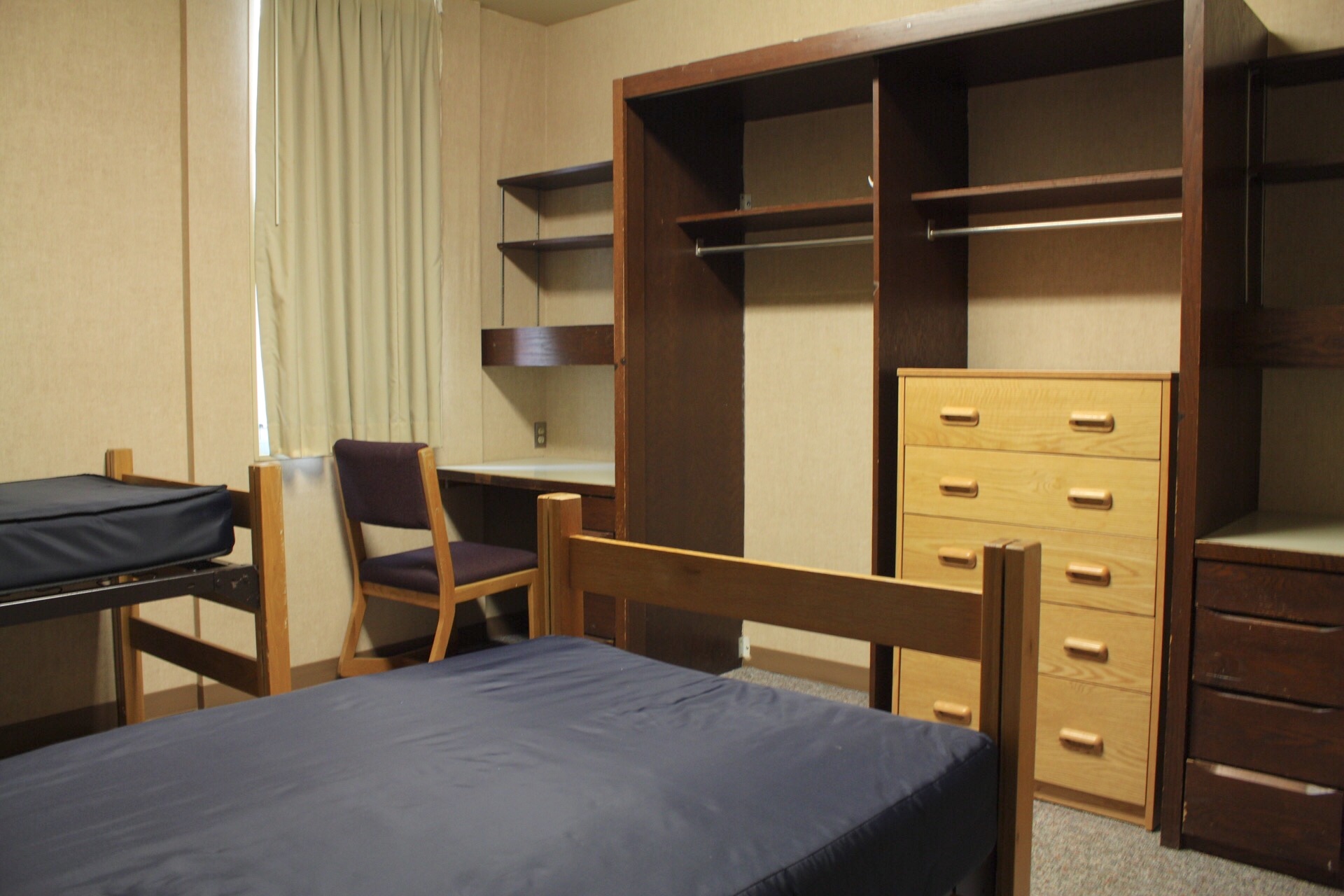 Centennial Complex with 2 bed frames, mattresses, a chair, a tall dresser, clothing hanging areas and shelves.