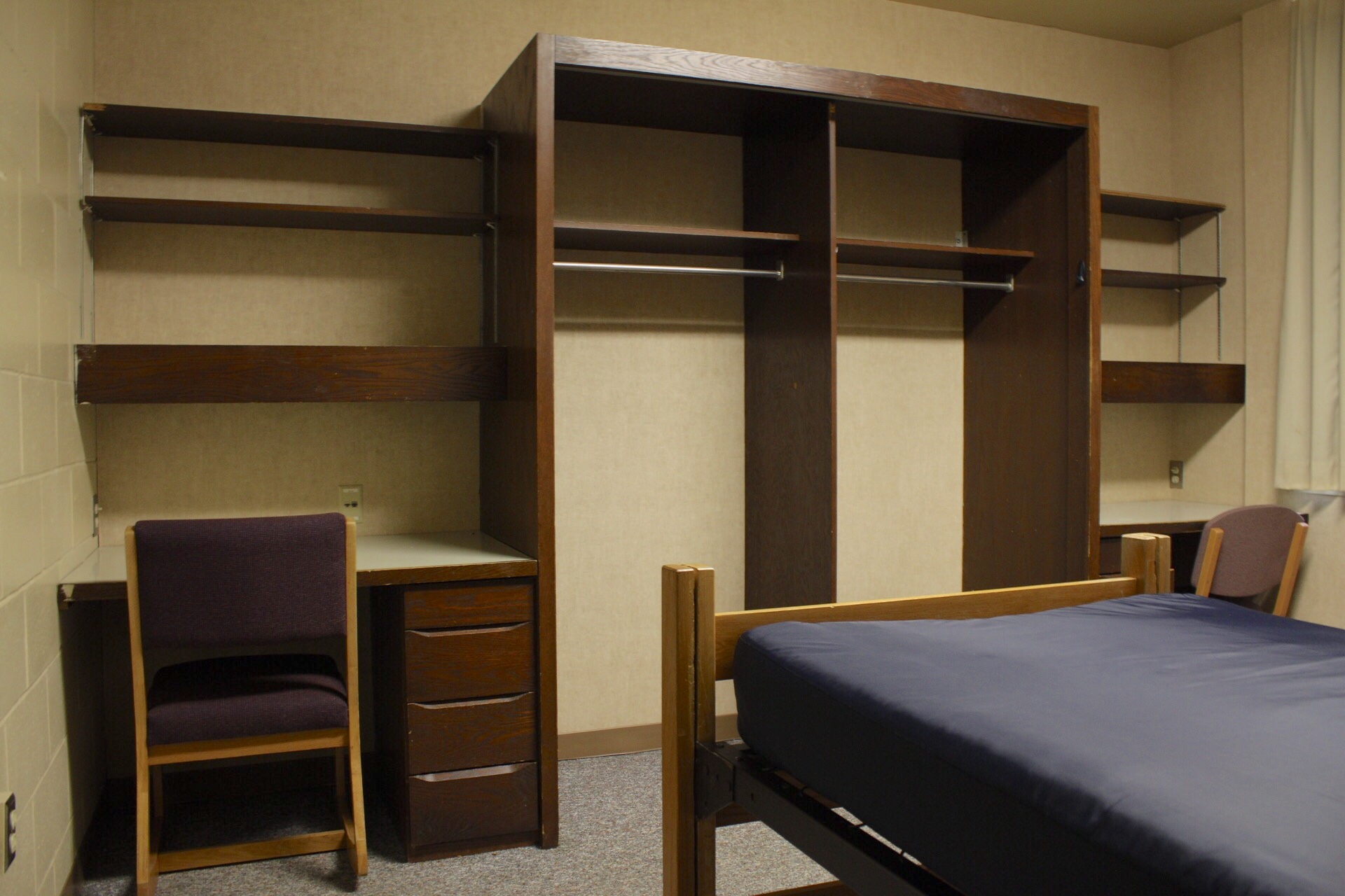 Centennial Complex room with 2 desks, 2 chairs, 2 hanging clothing hutches, shelves and a bed frame and mattress.