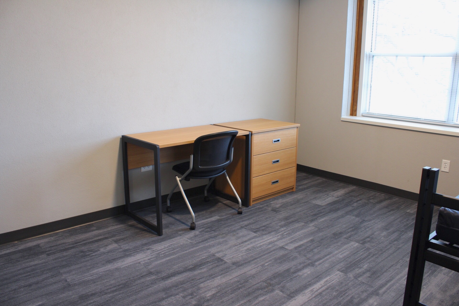 Delzell Hall room with a desk table, chair and 3-drawer dresser located near a large window.