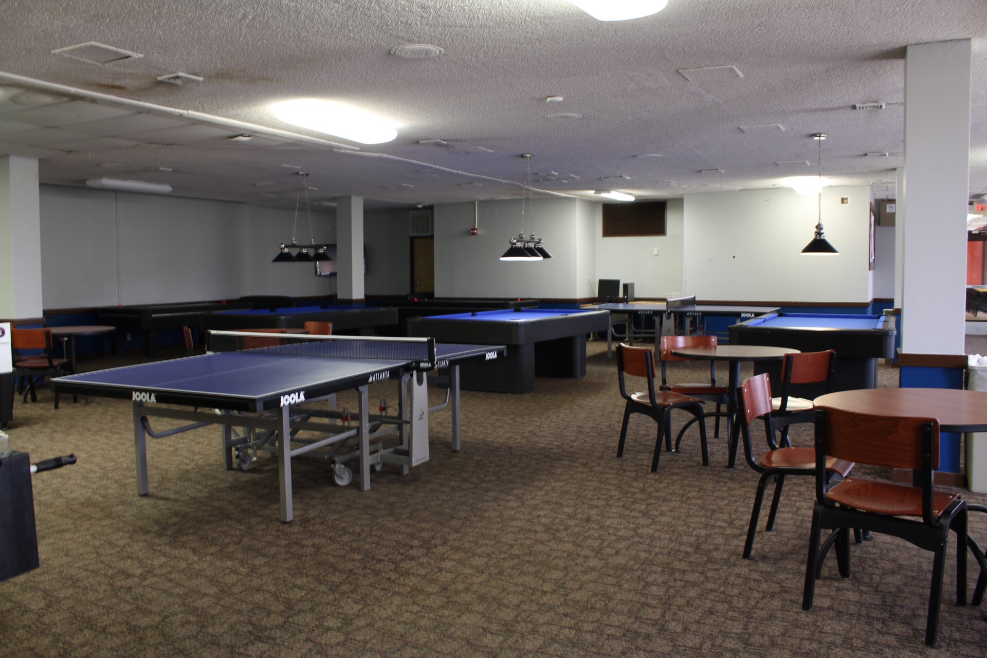 Wider shot of the game room showing 2 ping pong tables, tables and chairs, 3 pool tables, couches and wall mounted tv's.