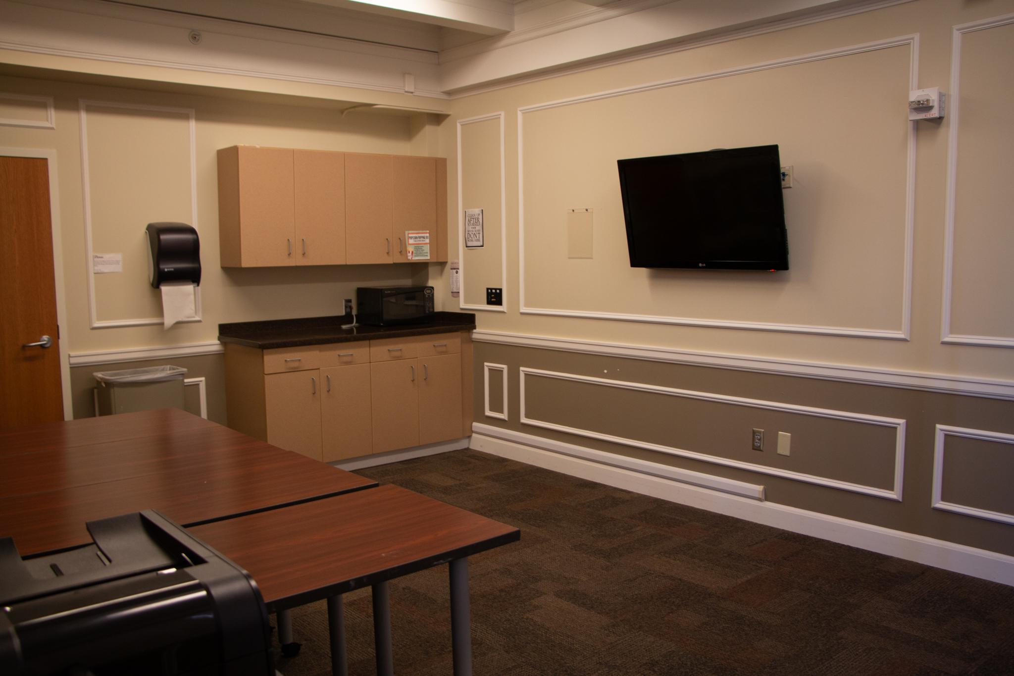 Morgan conference room with sink, wall mounted flatscreen tv and tables.