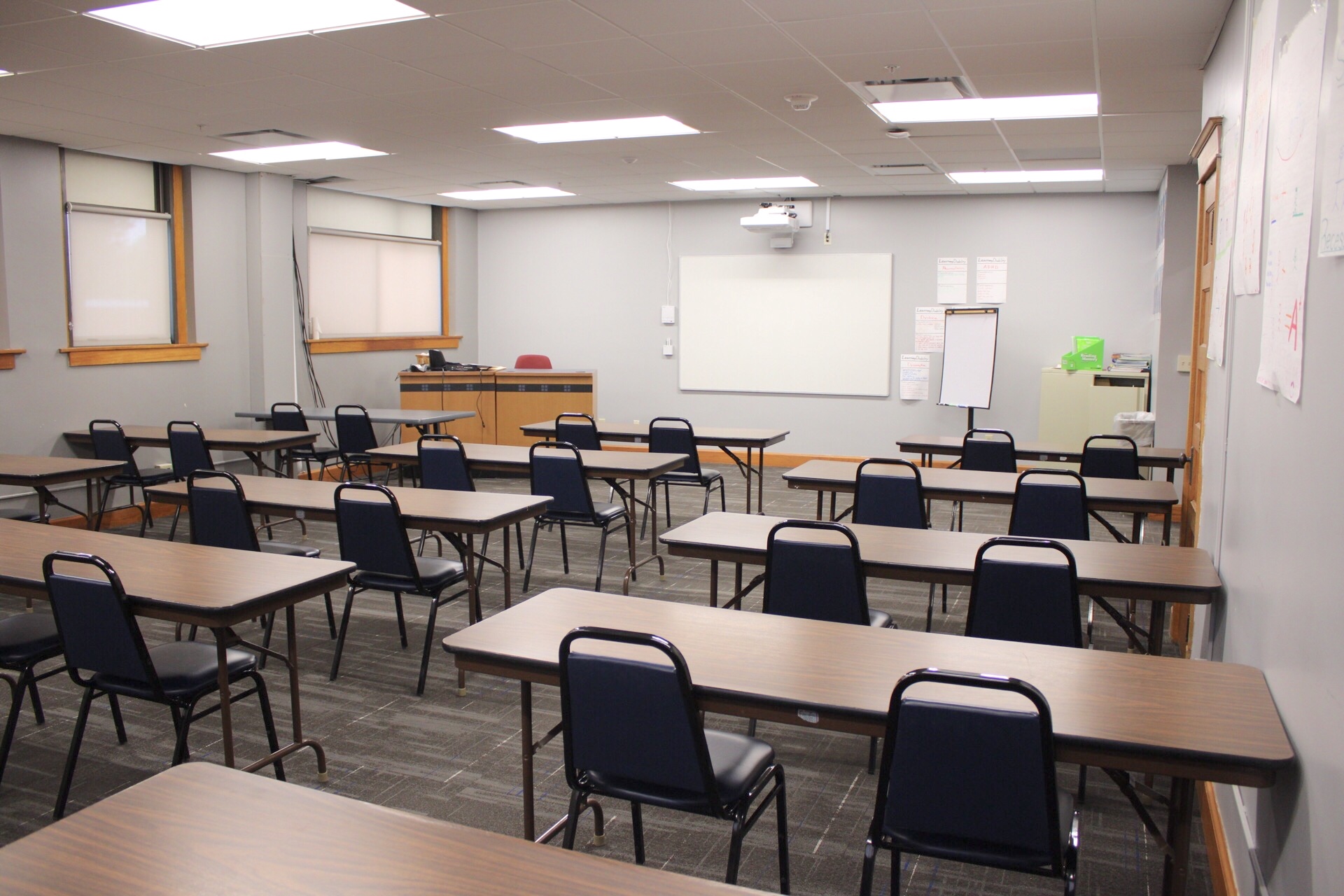 TJ Majors lecture 104 has tables, chairs, a wall mounted projector, whiteboard and a/v cart.