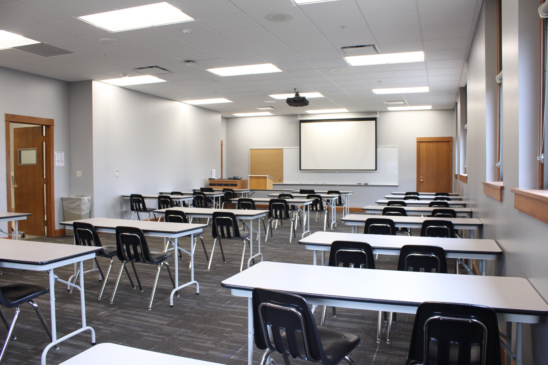 TJ Majors 326 has tables, chairs, an a/v cart, a portable podium, a large combination whiteboard/bulletin board, a ceiling mounted projector and a white projection screen.