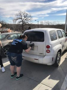 Student dusting the back hatch of a white car for finger prints.