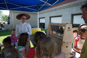 Nikki Hayes, in a traditional bee keeping outfit, explains her work at Aunt Bea's Apiary as children inspect a hive and other bee-keeping equipment.